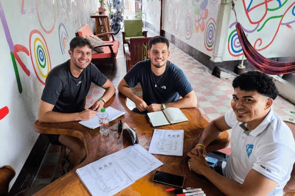 Two students seated with a tutor in a cozy classroom setting, engaged in a semi-private language lesson.